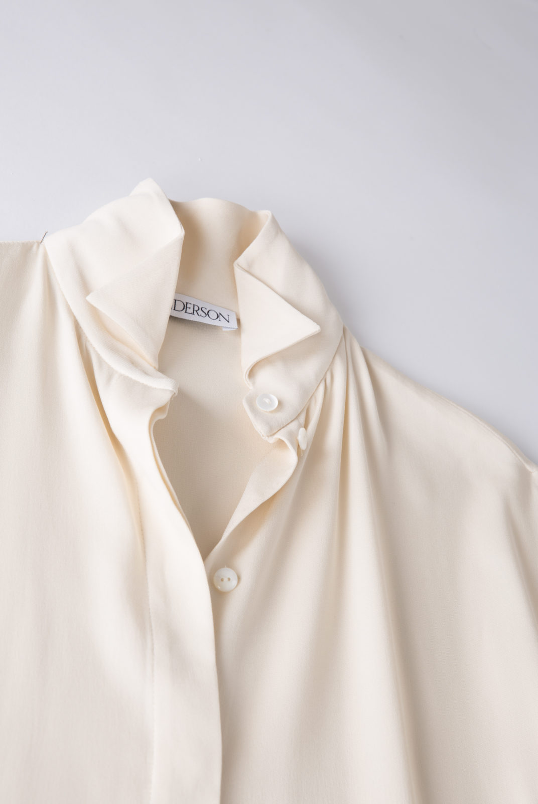 Blouse cream, en tissu double georgette, fluide et féminin, col souple et poignets ouverts, JW Anderson.