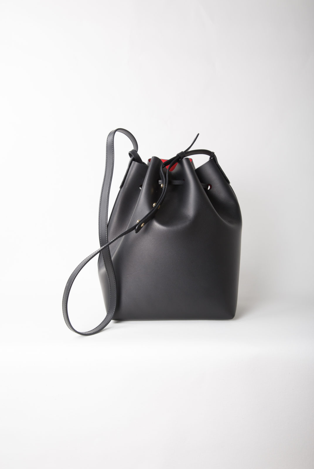 Sac seau italien en cuir tanné végétal noir avec intérieur vernis mat rouge. Sangle réglable. Fabriqué en Italie.